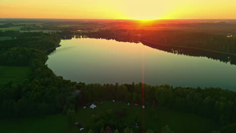 Stunning-aerial-drone-dolly-above-calm-pine-tree-lake-at-sunset,-red-yellow-glow-in-sky