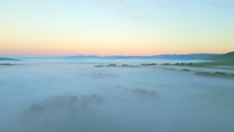 Nebel-Bedecktes-Land-Im-Morgengrauen-Mit-Langsamem-Schwenk-über-Die-Landschaft-In-Der-Höhe,-Der-Felder-Und-Berge-In-Der-Ferne-Zeigt