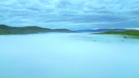 Flying-high-over-fog-bank-with-cloudy-sky-and-distant-mountains-at-dawn