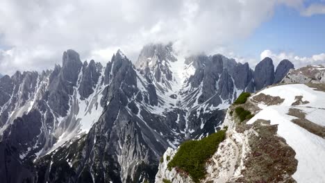 Una-Afilada-Cresta-De-Montaña-Rocosa-Que-Se-Eleva-Sobre-Un-Increíble-Valle-Verde-Con-Nieve
