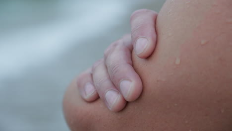 Close-Up-Shot-of-Man's-Hand-Resting-Against-Bare-Hip-by-the-Sea-on-a-Grey-Morning-Beach