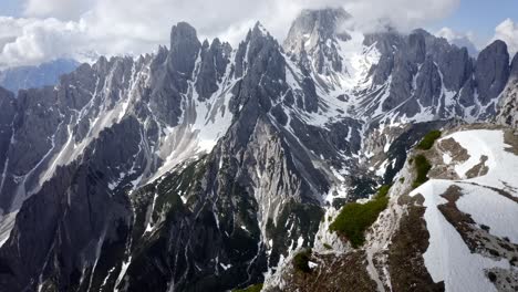 Una-Afilada-Cresta-De-Montaña-Rocosa-Que-Se-Eleva-Sobre-Un-Increíble-Valle-Verde-Con-Nieve