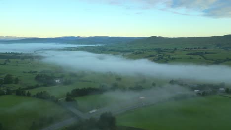 Flying-over-misty-M6-motorway-towards-green-hills-and-fog-bank-at-sunrise