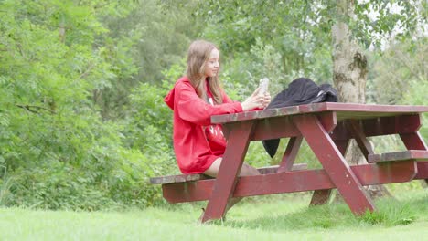 Young-happy-girl-sitting-outside-on-a-wooden-bench-making-video-call