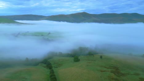 Flying-over-English-countryside-towards-misty-fog-bank-and-mountains-at-sunrise