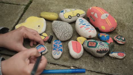 Female-hands-drawing-colorful-shapes-on-stones-with-markers