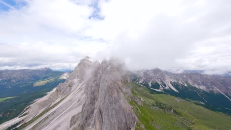 FPV-drone-flying-from-the-clouds-backwards-in-Seceda-mountain-ridge-located-in-Dolomite-Mountains,-Italian-Alps