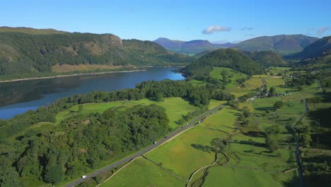 Pan-of-green-valley-with-lake,-mountains-and-busy-road-on-sunny-summer-morning-at-Thirlmere,-English-Lake-District,-UK