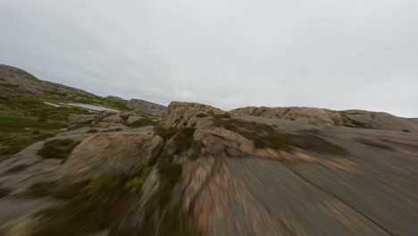 FPV-drone-proximity-flight-over-edges-of-cliffs-and-a-small-lake-in-Ramsvik,-Sweden