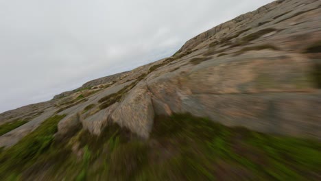 FPV-drone-flying-low-over-rocks-and-cliffs-on-a-cloudy-day-in-Ramsvik,-Sweden