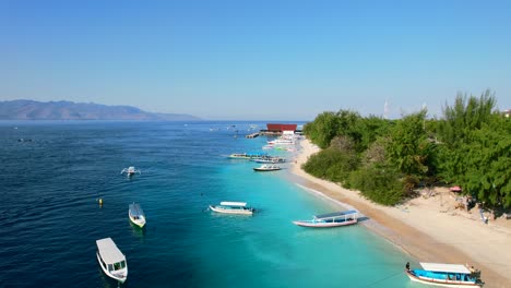 Travel-Tour-Boats-Moored-on-Gili-Trawangan-Island-Soft-Sand-with-Idyllic-Turquoise-Sea-in-Indonesia---aerial-pull-back