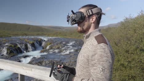 Man-with-FPV-goggles,-controlling-drone-near-Icelandic-river-landscape