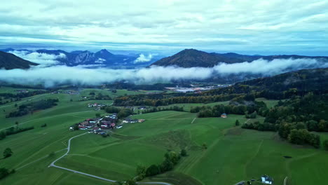 Aerial-shot-of-the-green-landscape-with-mist-and-clouds-surrounding-the-mountain-peaks-in-the-far-distance
