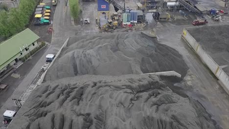 Vista-Aérea-Del-Stock-De-Agregados-En-Forma-De-Arena,-Grava-Y-Relleno-En-Una-Planta-De-Asfalto-Cerca-De-La-Planta-Mezcladora-De-Asfalto,-Construcción-De-Maquinaria-Y-Otros-Equipos-De-Construcción-Pesados