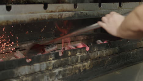 Der-Koch-Schürt-Das-Feuer-Mit-Einem-Schürhaken-Und-Schiebt-Glühende-Kohlen-Beiseite