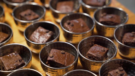 Slices-of-square-shaped-chocolate-cake-in-small-bowls-lined-up-on-a-table