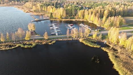 Schweden-–-Ein-Herbstlicher-Wald-An-Einer-Ruhigen-Bucht-Mit-Angedockten-Booten-Und-Der-Untergehenden-Sonne,-Die-Ein-Warmes-Leuchten-Verbreitet-–-Drohnen-Weitwinkelaufnahme