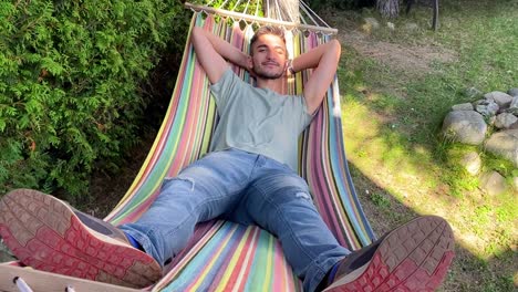 Close-up-shot-shot-of-a-casual-happy-boy-relaxing-on-a-colorful-hammock-in-an-outdoor-garden-on-holiday-on-a-sunny-day