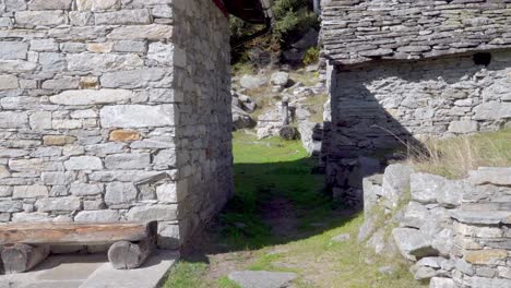 Rustic-stone-houses,-walls-and-a-roof,-a-wooden-bench-in-the-foreground-and-a-drinking-water-fountain-at-the-far-back-of-the-clip