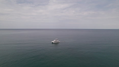 Half-orbit-drone-shot-focused-on-a-yacht-with-vast-sea-views,-ending-with-Careyeros-beach-and-Punta-de-Mita-coast