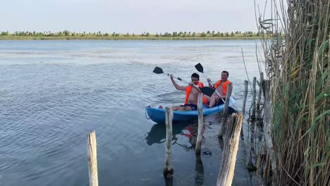 Foto-De-Dos-Hombres-Remando-Juntos-En-Un-Kayak-En-Un-Lago-De-Agua-Dulce-A-Lo-Largo-Del-Campo-Rural-En-Bucarest,-Rumania-Durante-El-Día