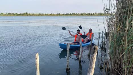 Shot-of-two-men-paddling-together-on-a-kayak-in-a-fresh-water-lake-along-rural-countryside-in-Bucharest,-Romania-at-daytime