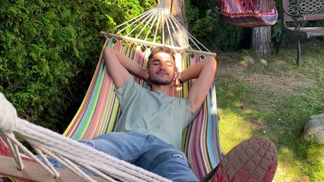 Close-up-shot-shot-of-a-casual-happy-boy-relaxing-on-a-colorful-hammock-in-an-outdoor-garden-on-holiday-on-a-sunny-day