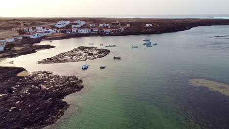 Flyover-of-Ajuy-with-residentials-and-boats-in-the-water,-Fuerteventura