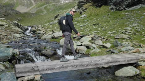 Male-Hiking-Across-Bridge-Crossing-River-On-Mountain-At-Valtellina,-Italy