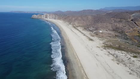 Aerial-view-of-an-idyllic-coastline-with-pristine-beach-while-the-waves-from-the-blue-sea-gently-crash-onto-the-shore-while-traveling-through-mexico-on-the-beachof-cabo-san-lucas-in-todos-santos