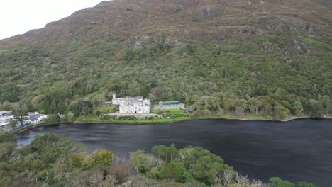 Aerial-view-of-the-historic-and-oldest-Benedictine-Abbey-the-Kylemore-Abbey-in-Connemara-Galway,-Ireland-overlooking-a-black-river-which-mirrors-the-abbey