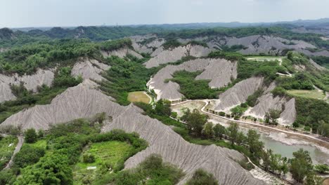 Ascending-drone-shot-of-Tianliao-Moon-World-landscape-with-trail-and-green-hills-during-cloudy-day
