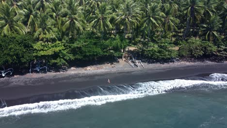 Geheime-Oase:-4K-Luftaufnahme-Einer-Umlaufenden-Drohne-Eines-Einsamen-Mädchens,-Das-Am-Unberührten-Schwarzen-Sandstrand-In-Gretek,-Bali,-Liegt