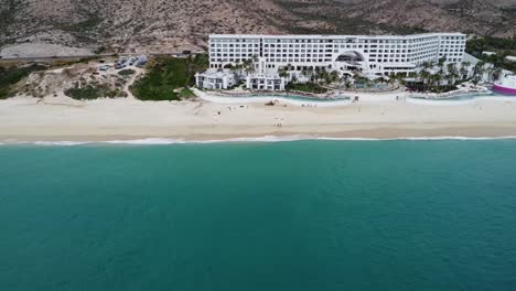 Aerial-panning-view-of-the-beautiful-coastal-shoreline-in-los-cabos-with-a-view-of-the-sandy-beach,-a-busy-coastal-road-and-the-turquoise-sea-and-the-renowned-Marquis-hotel-during-a-mexico-vacation