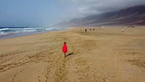 Woman-walking-on-a-vast-beach-with-the-blue-ocean-and-mountain-scenery