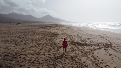 Eine-Frau-Geht-Allein-An-Einem-Sonnigen-Strand-Von-Fuerteventura-Mit-Dunstigem-Himmel-Spazieren