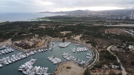 Aerial-view-of-a-beautiful-harbor-with-boats-and-yachts-at-a-bay-of-the-coast-in-Marina-Puerto-Los-Cabos-in-mexico-with-a-view-of-dry-coastal-landscape,-the-blue-sea-and-mountains-in-the-background