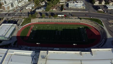 Rotating-wide-aerial-drone-shot-of-an-American-high-school-football-stadium-and-track-next-to-a-busy-street-on-a-warm-sunny-fall-evening-in-Salt-Lake-county,-Utah