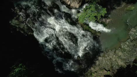 Aerial-drone-top-down-shot-over-a-multilevel-unique-waterfall-surrounded-by-green-vegetation-at-daytime