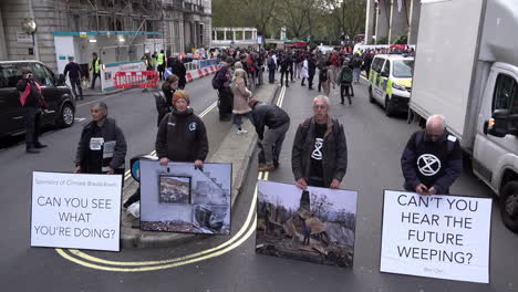 Aktivisten-Der-Extinction-Rebellion-Blockieren-Eine-Straße-Mit-Fotoplakaten,-Die-Katastrophen-Des-Klimawandels-Darstellen,-Im-Intercontinental-Hotel-In-Mayfair,-Wo-Das-Energy-Intelligence-Forum-Stattfindet