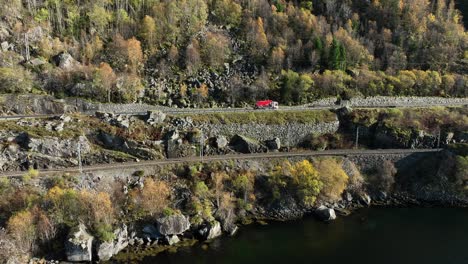Red-and-white-truck-driving-towards-Bergen-below-steep-hillside-at-road-E16-in-Stanghelle,-Norway