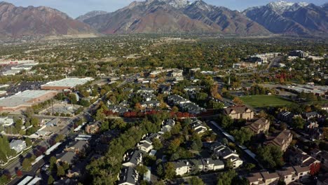 Tilt-up-dolly-in-aerial-drone-wide-landscape-shot-revealing-the-stunning-snowcapped-rocky-mountains-of-Utah-with-Salt-Lake-county-below-full-of-buildings-and-colorful-trees-on-a-warm-sunny-fall-day