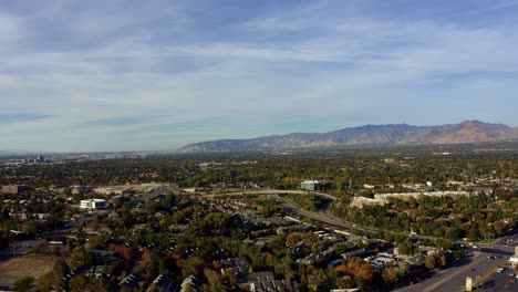 Right-trucking-rising-aerial-drone-extreme-wide-landscape-shot-of-the-Salt-Lake-county-valley-covered-in-buildings,-busy-roads,-and-colorful-autumn-trees-on-a-warm-sunny-fall-evening-in-Utah