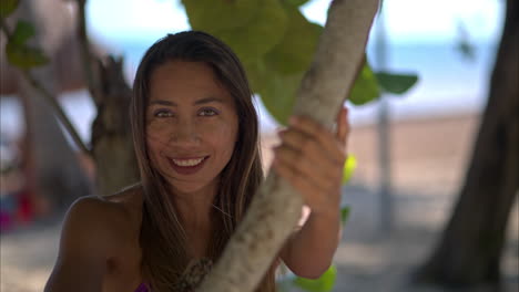 Junge-Schöne-Lateinamerikanische-Hispanoamerikanerin-Neckt-Lächelnd-In-Die-Kamera-An-Einem-Wunderschönen-Strand-In-Mexiko,-Während-Der-Wind-Ihr-Die-Haare-Weht