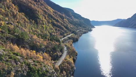 Road-E16-Stanghelle-at-bottom-of-mountainous-autumn-colored-hillside-and-Sorfjorden-sea-beside,-Norway-aerial