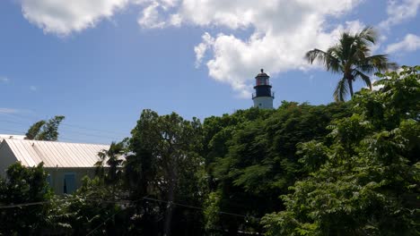 Key-West-Lighthouse-amidst-tropical-trees,-blue-sky-backdrop,-Florida