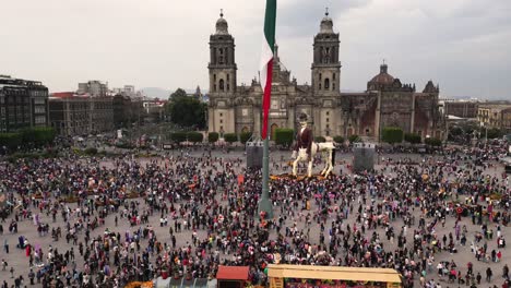 drone-hyperlapse-video-capturing-a-crowd-walking-through-Mexico-City's-Zocalo,-featuring-the-national-flag-and-the-city's-cathedral