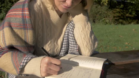 Woman-wearing-sweater-writing-at-park-bench