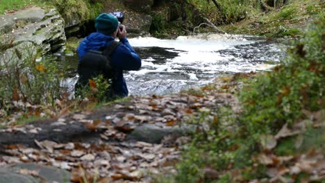 A-young-boy,-equipped-with-a-camera-and-tripod,-photographs-the-peaceful-autumn-winter-woodland-and-its-meandering-stream