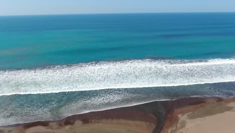 Costa-Rica-beach-drone-flying-over-the-shore-and-into-the-ocean-with-a-river-opening-to-the-water-on-the-pacific-ocean-on-a-sunny-day